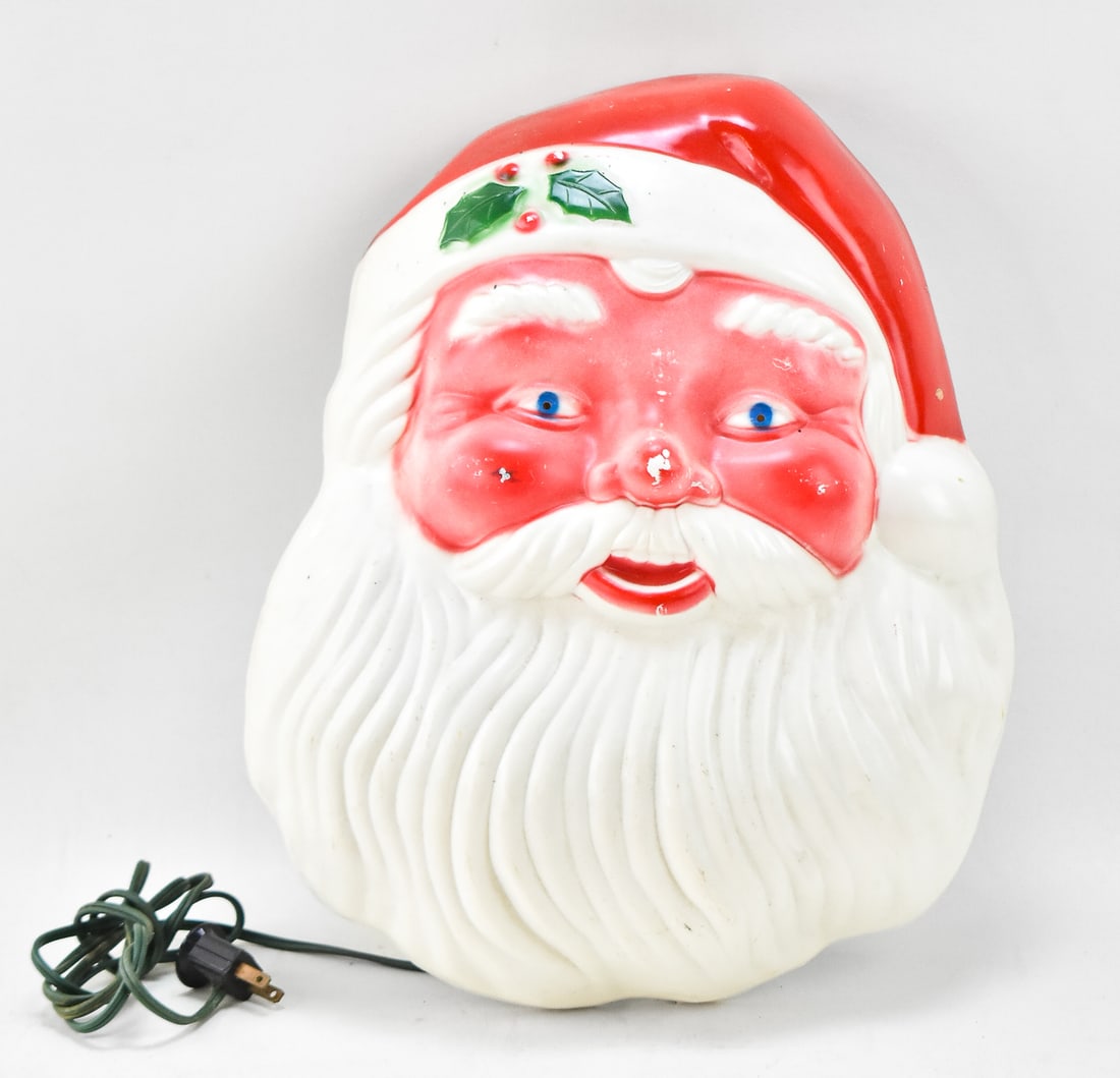 VINTAGE NOMA SANTA CLAUS FACE LIGHT-UP WALL DECOR: A NOMA hard plastic light-up Christmas wall decor featuring Santa Claus's face, circa 1950-1960s. The item measures 15" H, 12" W, 5" D.