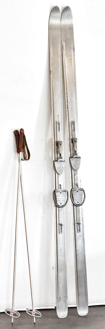 VINTAGE TEY MANUFACTURING COMPANY TRUE-HOLD ALUMINUM SKIS & POLES: A Tey Manufacturing Company pair of True-Hold aluminum skis with poles, circa early to mid 20th century. The item measures 84" H, 4.5" W, 4" D.
