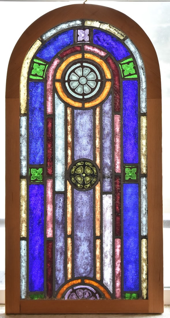 ARCHED STAINED GLASS WINDOW PANEL: An antique arched stained glass window panel with rosette design in wooden frame with top hook, measuring 31.5" H x 15.5" W x 1" D.