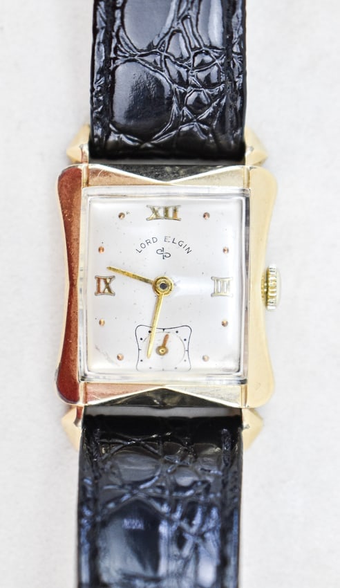 LORD ELGIN 14K GOLD-FILLED WATCH: A Lord Elgin 14k gold-filled wristwatch with a sub-second movement, circa 1950s. The watch comes with a black leather band. The watch case measures 1.5" H x 1" W x 1.35" D.