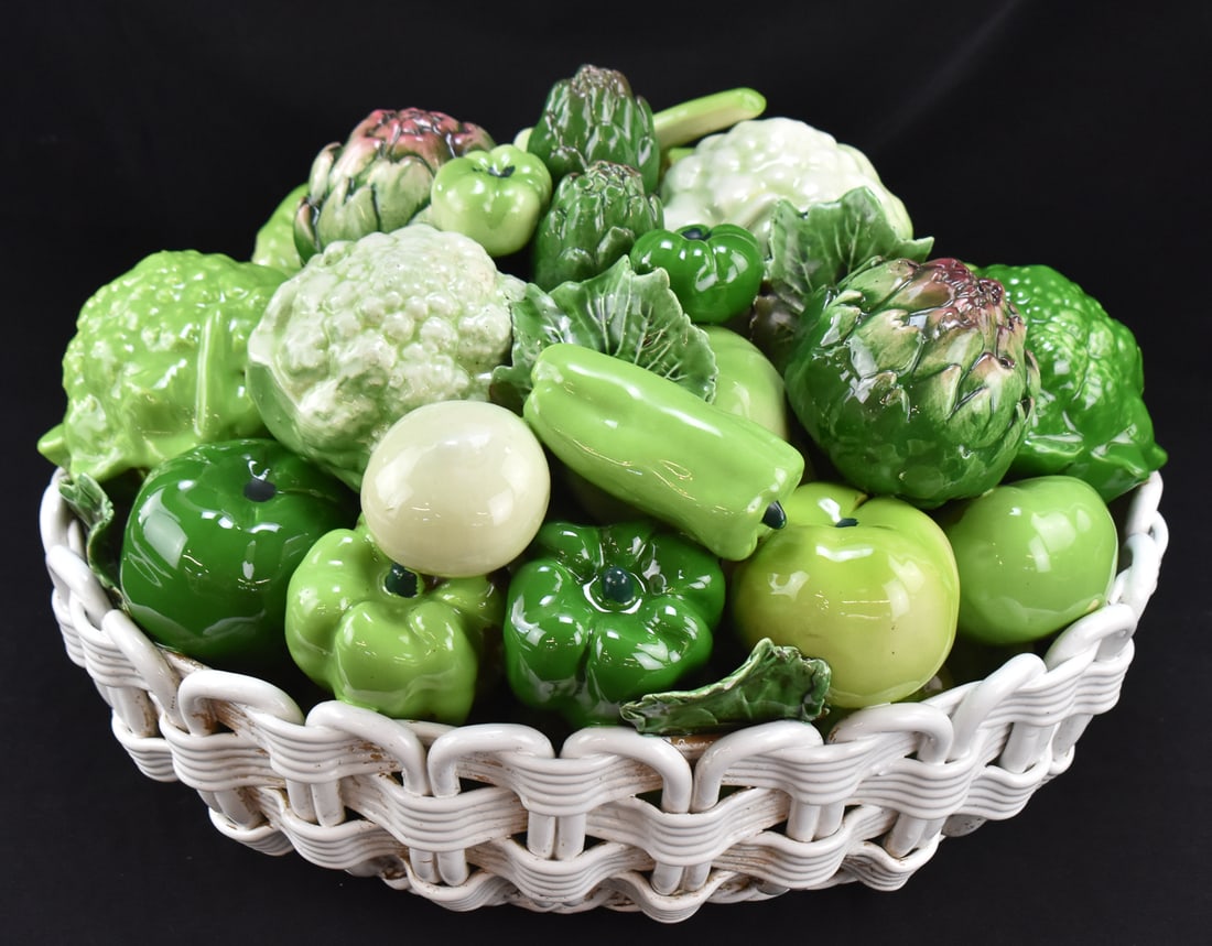 MAJOLICA STYLE ITALIAN CERAMIC VEGETABLE BASKET: A Majolica style Italian ceramic centerpiece of a vegetable gathering in a braided basket, circa mid to late 20th century. The item measures 11" H, 16.5" W, 13" D.