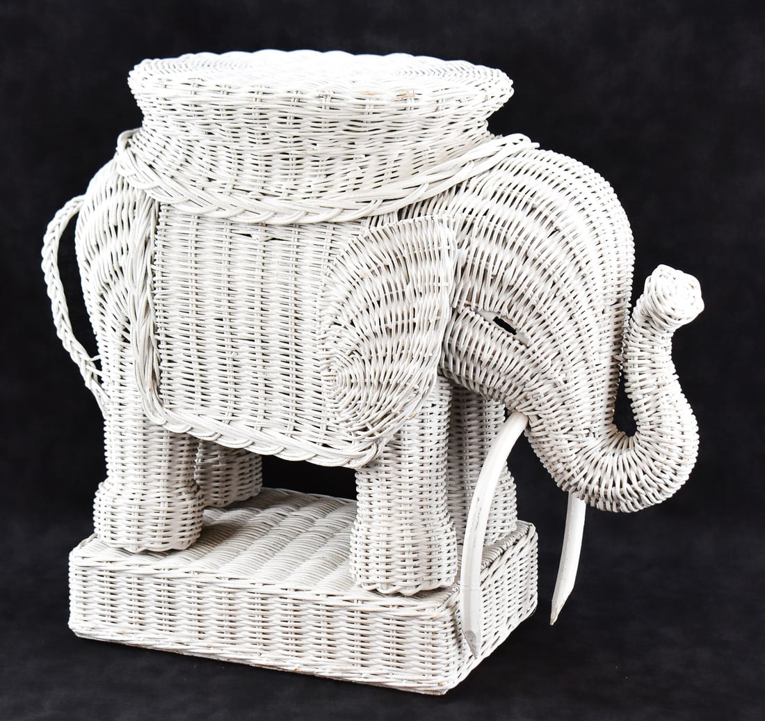 MID-CENTURY WHITE WICKER ELEPHANT PLANT STAND OR SIDE TABLE: A Mid-century white wicker elephant plant stand or side table with wooden tusks, hand-painted eyes, and a wooden base 16.5" H x 19" W x 7.5" D.