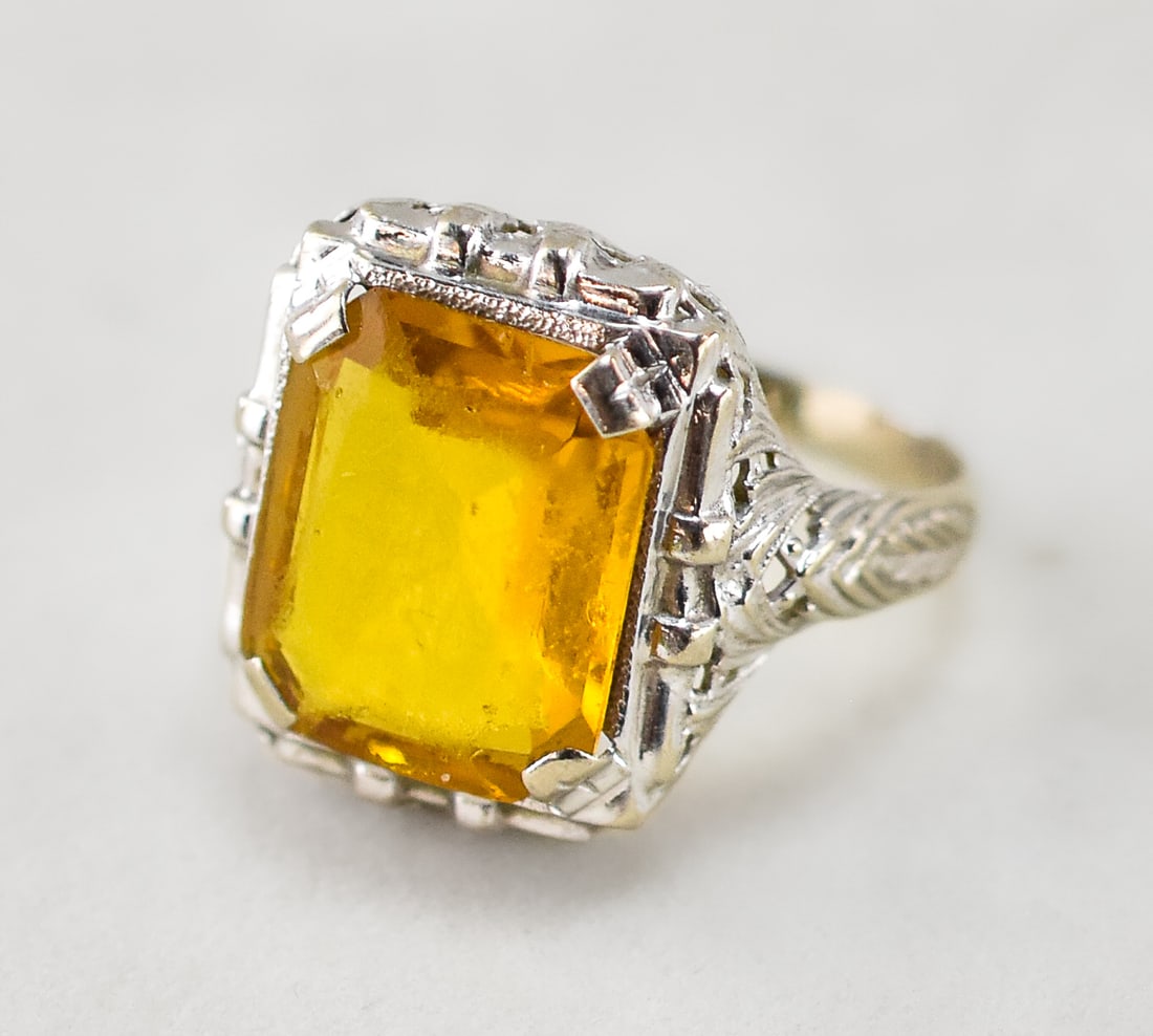 10K WHITE GOLD RING WITH GLASS STONE: A 10K white gold ring with an orange/yellow glass set stone. The ring is marked 10K on the inside of the band and has been confirmed 10K gold through professional testing. The ring has a weight of