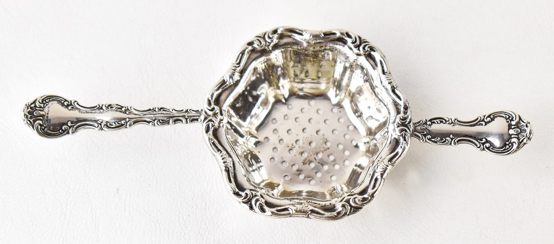 BINKS 'POMPADOUR' STERLING SILVER OVER-CUP TEA STRAINER: A Binks "Pompadour" sterling silver over-cup tea strainer. The tea strainer has a weight of 32 grams and measures 0.75" H x 6" W x 2.5" D.