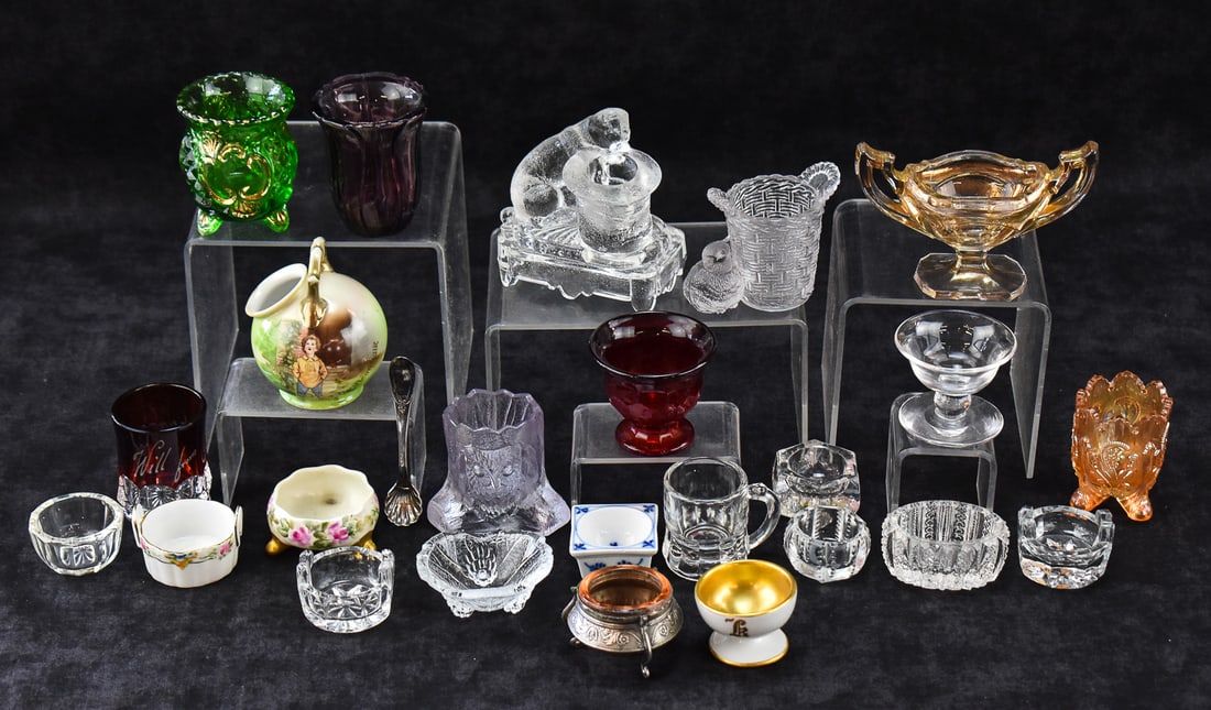 COLLECTION OF TOOTHPICK HOLDERS, SALT CELLARS, & MORE: A collection of twenty-five vintage and antique glass and porcelain toothpick holders, salt cellars plus one silver salt spoon. The largest of the collection is the Belmont Glass Works dog toothpick