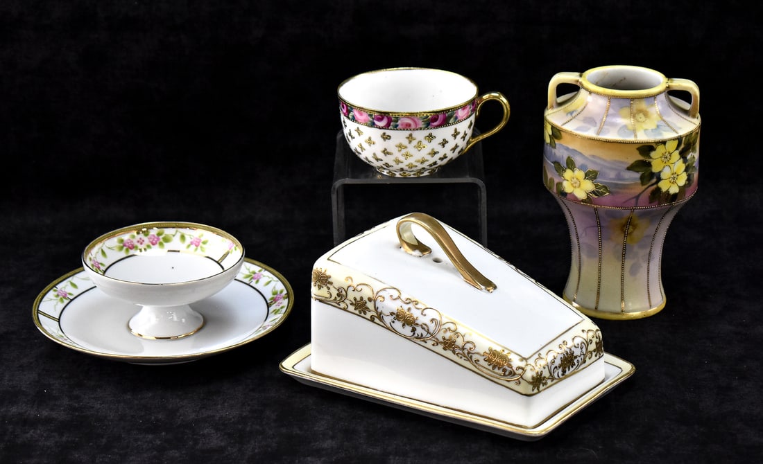 NIPPON CHINA ASSORTMENT: An assortment of hand-painted Nippon chinaware including a two-tiered serving dish with pink floral patterns, a teacup with pink roses and gold detailing, a gold on white cheese keep, and a handled va