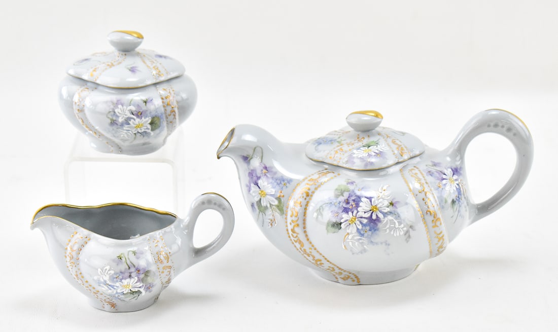 ROYAL CREST HAND-PAINTED FINE BONE CHINA TEA SERVICE: A Royal Crest hand-painted light blue fine bone china tea service, numbered and signed "A Powel". Includes a 4.5" H x 9" W x 5.5" D lidded teapot, creamer pitcher and a lidded sugar bowl.