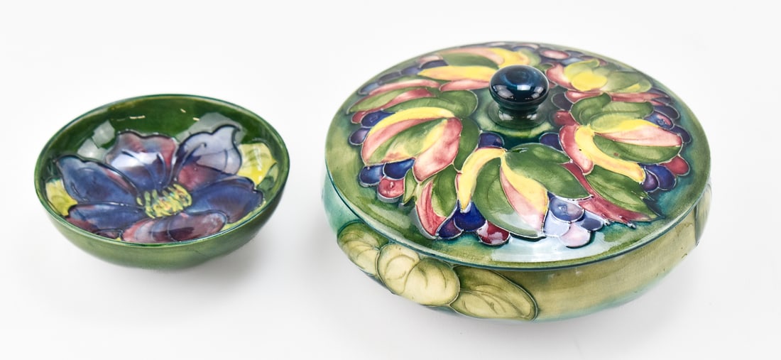 WILLIAM MOORCROFT 'CLEMATIS' & 'LEAVES AND FRUIT' BOWLS: A William Moorcroft "Clematis" footed bowl and a lidded "Leaves and Fruit" pattern bowl, circa early 20th century. The largest item measures 4" H, 6.5" W, 6.5" D.