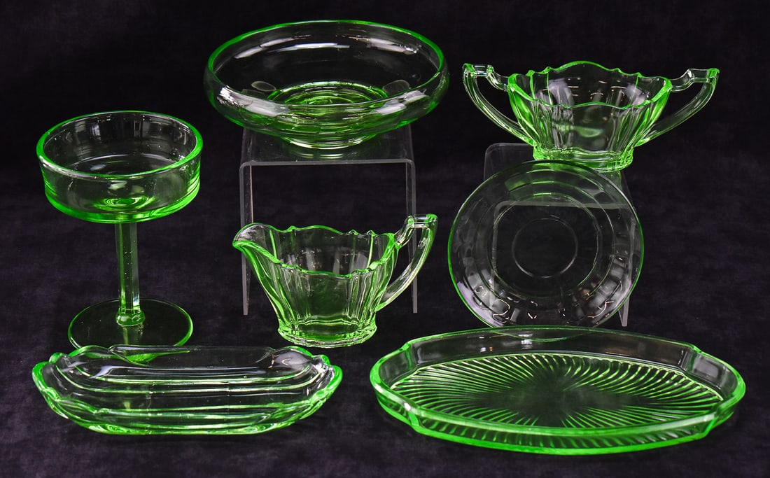 COLLECTION OF URANIUM GLASS: A collection of seven pieces of uranium glass which includes a small plate, a footed bowl, a relish tray, a butter tray, a sugar and creamer set and a stemmed coupe-style glass measuring 6"H x 4.75"W