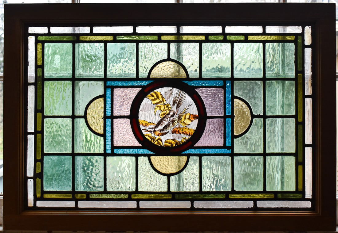 ENGLISH VICTORIAN LEAD STAINED GLASS WINDOW PANEL: REDWING-LIKE BIRD: An English Victorian lead stained glass window panel featuring possibly a Redwing bird within a contemporary wooden housing, circa late 19th century. The item measures 21.5" H, 32" W, 1.5" D.