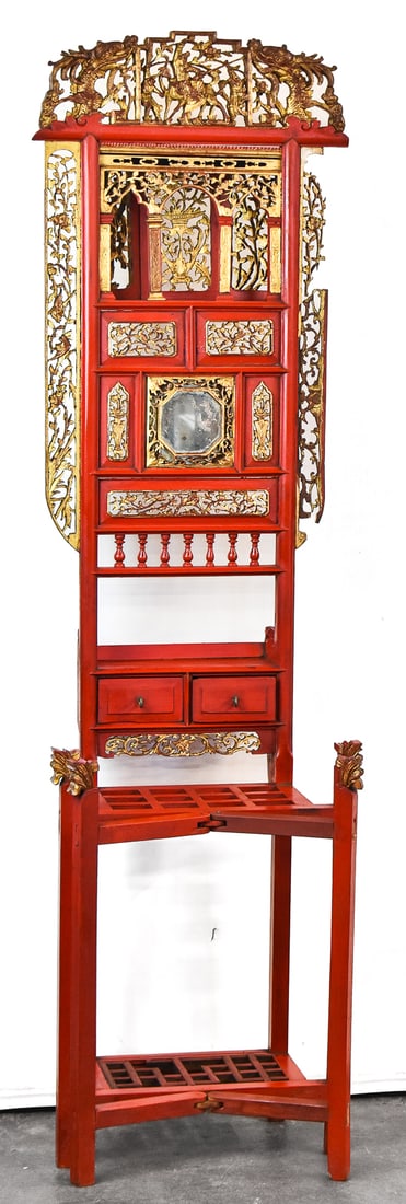 CHINESE WASH STAND; EARLY 20TH CENTURY: A Chinese red-painted and gilt wash stand featuring carved and pierced panels, two short drawers, folding legs, circa early 20th century. The item measures 70" H, 19.5" W, 13.5" D.