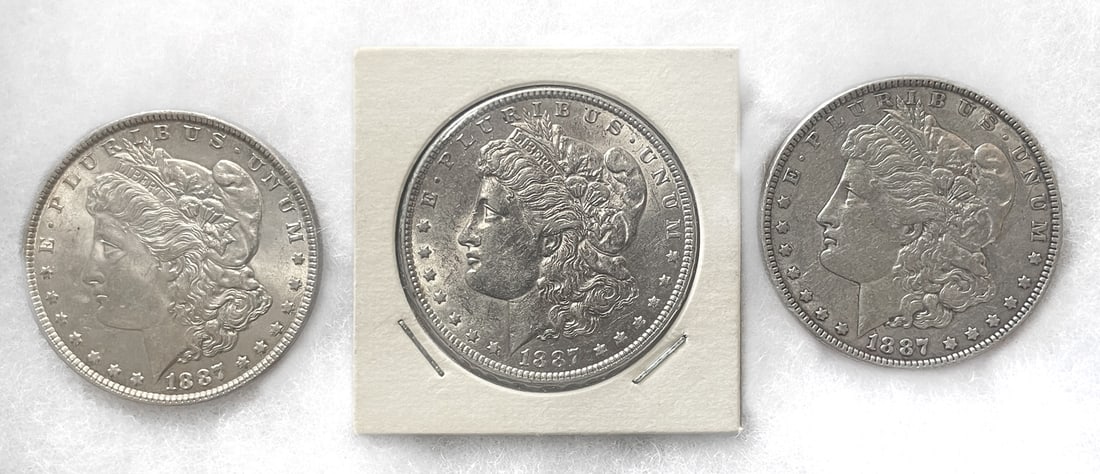 THREE 1887 MORGAN SILVER DOLLARS: Three 1887 U.S. Morgan silver dollars minted in Philadelphia. One of the coins is kept in a paper coin flip. Each silver dollar is struck in 90% silver with each having a weight of approximately 26.7