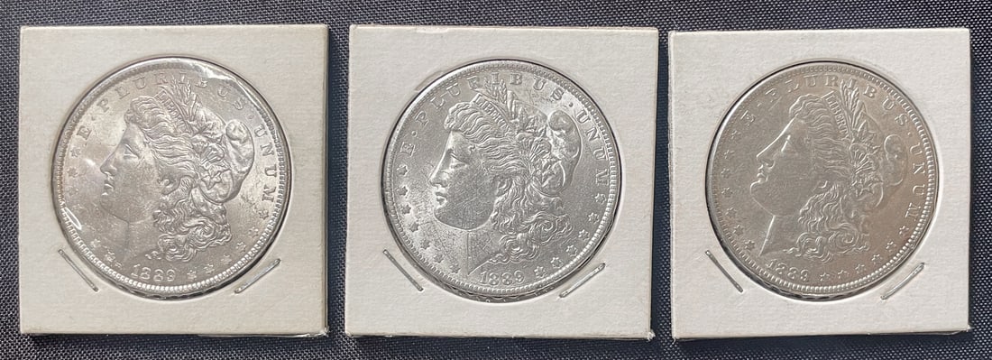 THREE 1889 MORGAN SILVER DOLLARS: Three 1889 U.S. Morgan silver dollars minted in Philadelphia. Each coin his held in a paper coin flip. Each silver dollar is struck in 90% silver with each having a weight of approximately 26.7 grams.