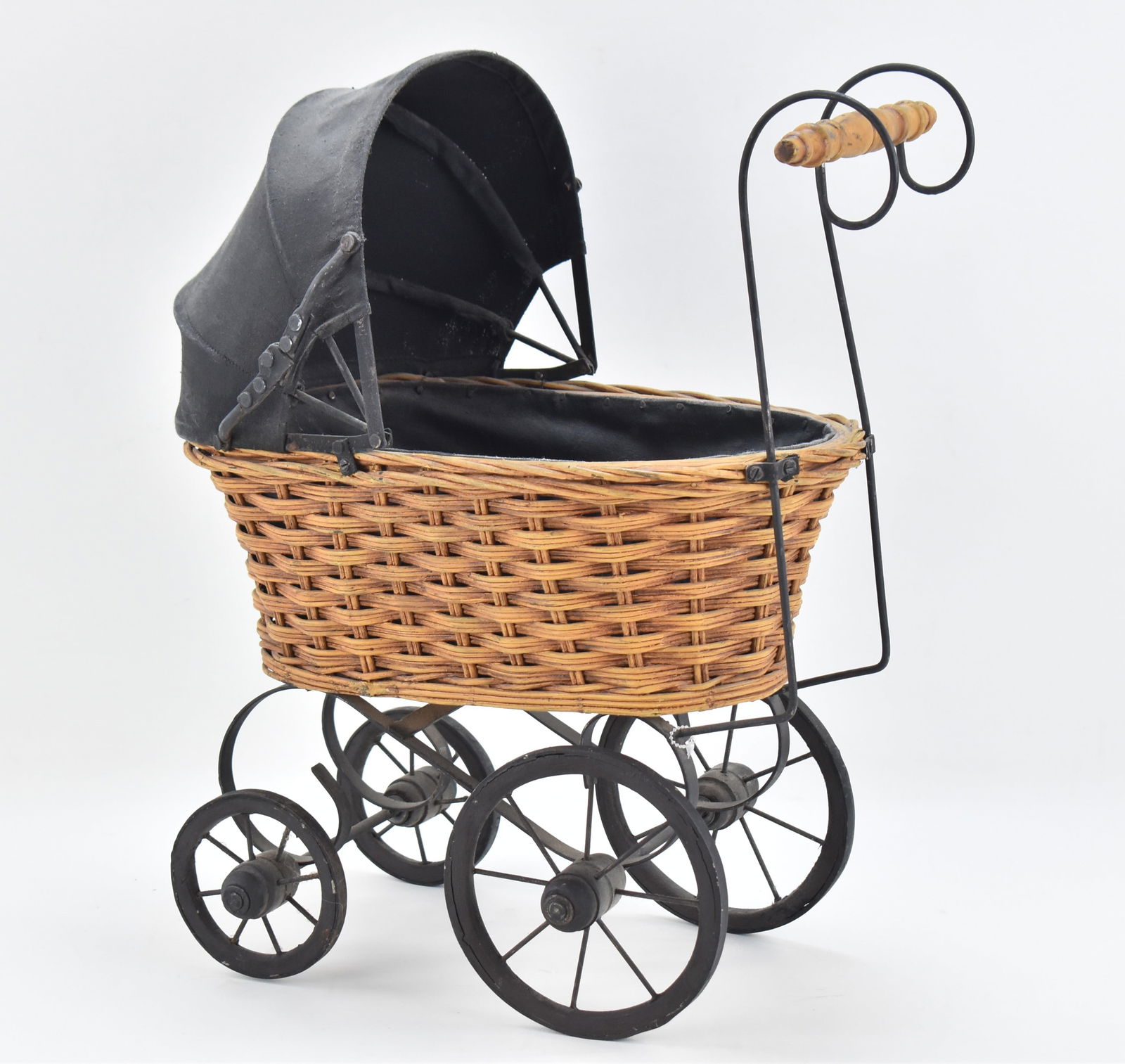 VICTORIAN WICKER BABY DOLL CARRIAGE: A Victorian wicker baby doll carriage with a black fabric canopy, cast iron frame and wooden wheels, circa mid-20th century. The carriage measures 19" H x 9" W x 15" D.