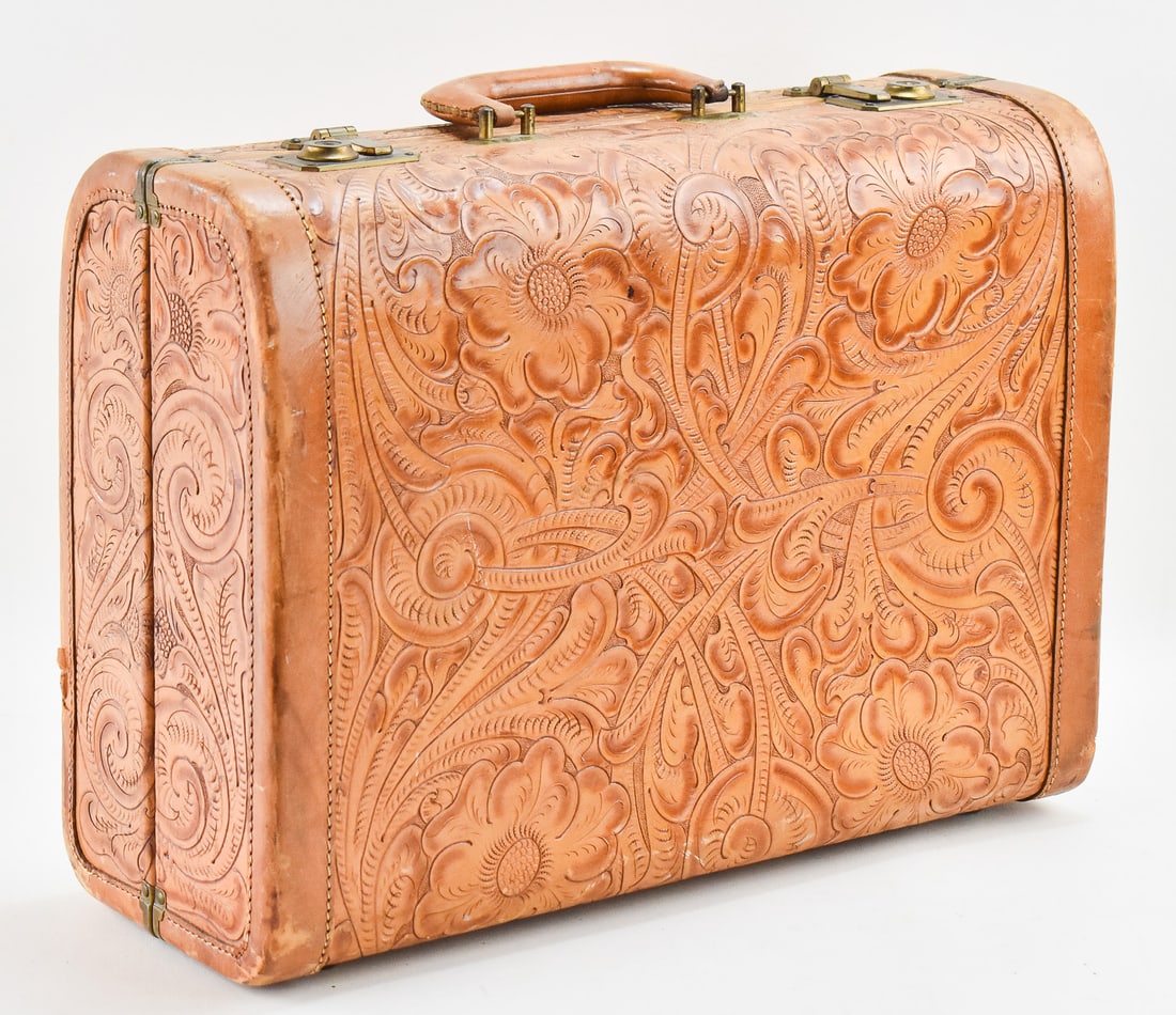 VINTAGE HAND-TOOLED FLORAL DESIGN LEATHER SUITCASE: A vintage brown leather suitcase with an intricately hand-tooled floral design measuring 14" H x 19" W x 7.25" D.