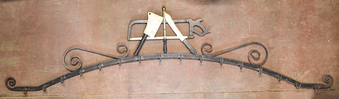 BERNARD GLOEKLER COMPANY WROUGHT CAST IRON BUTCHER'S MEAT RACK: A Bernard Gloekler Company wrought and cast iron butcher's meat rack stylized with butcher's tools and 16 hooks, circa 1880s. The item measures 26" H, 96.5" W, 2.5" D.
