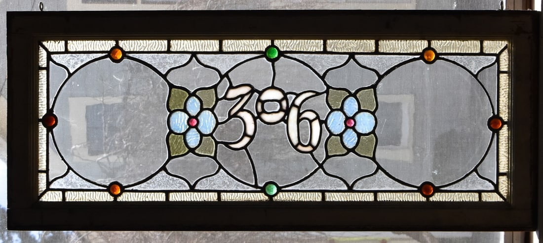 ANTIQUE LEADED STAINED GLASS WINDOW PANE IN FRAME: An antique leaded stained glass window pane in a window frame. The window frame has two eye bolts on the top so the window can be hung and displayed. The window pane has an interior floral design and