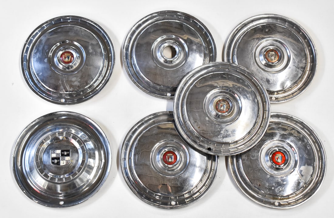 FORD & STUDEBAKER HUBCAPS: An assortment of seven hubcaps including 5 vintage Ford hubcaps, a Studebaker hubcap, and one hubcap missing the center emblem. The Studebaker hubcap measures 15" H x 15" W x 2" D.
