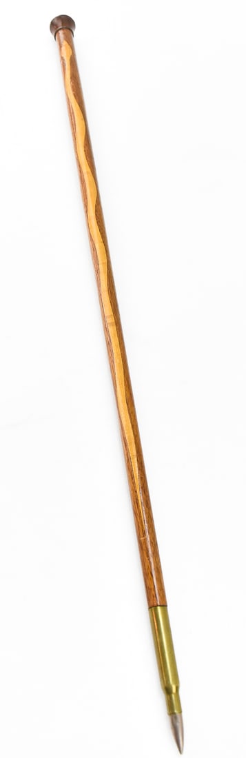 SHORT TRENCH ART STAFF: A short wooden staff with an inlaid light wood snake pattern and a bullet casing with bullet for the tip of the staff. A piece of post-war trench art. The staff measures 26" H x 1.25" W x 1.25" D.