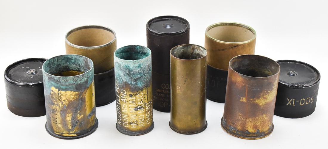 INERT BLANK HOWITZER SHELLS: An assortment of four howitzer shells, three of which are kept in their original cases. A 75mm blank cartridge, a 105mm M14 in a cardboard tube, a 75mm M5A1 Type 1 dated 1943 in a cardboard tube, and