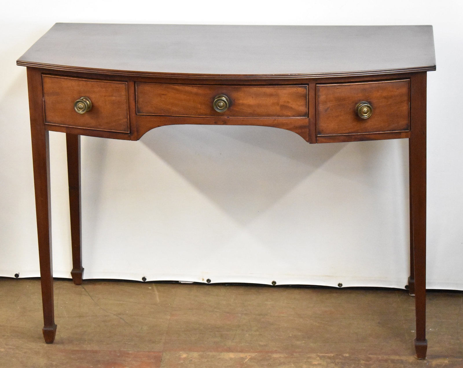 ENGLISH HEPPLEWHITE STYLE MAHOGANY SERVER: An English Hepplewhite style mahogany server with three drawers, bowed front, and tapered cuffed legs circa late 18th - early 19th century. The item measures 32.5" H, 43" W, 21" D.