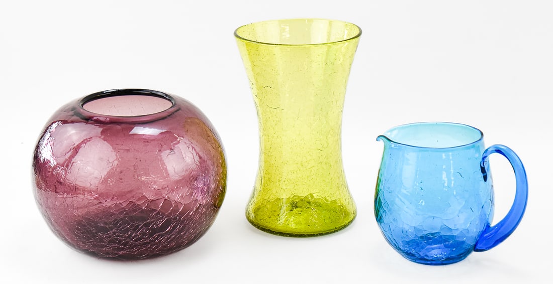 COLORFUL TRIO OF MID-CENTURY BLENKO CRACKLE GLASS: A colorful trio of Mid-century Blenko hand-blown crackle glass which includes a turquoise pitcher, a round amethyst vase, and a yellow vase measuring 9" H x 6" W x 6" D.