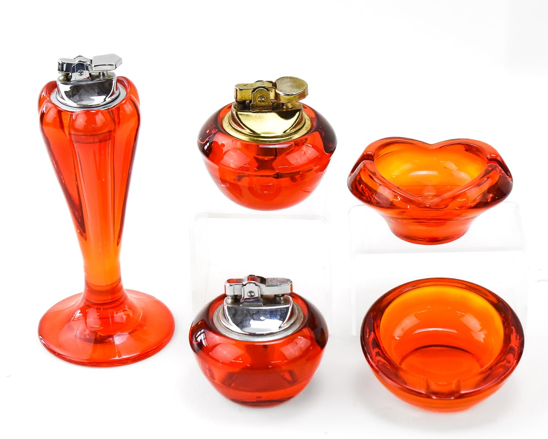 MID-CENTURY MODERN VIKING GLASS PERSIMMON ORANGE GLASS LIGHTERS & ASHTRAYS: An assortment of Mid-century Modern Viking Glass persimmon orange glass including a tall table lighter, two short table lighters, and two small ashtrays. The largest lighter measures 6.5" H x 3" W x 3