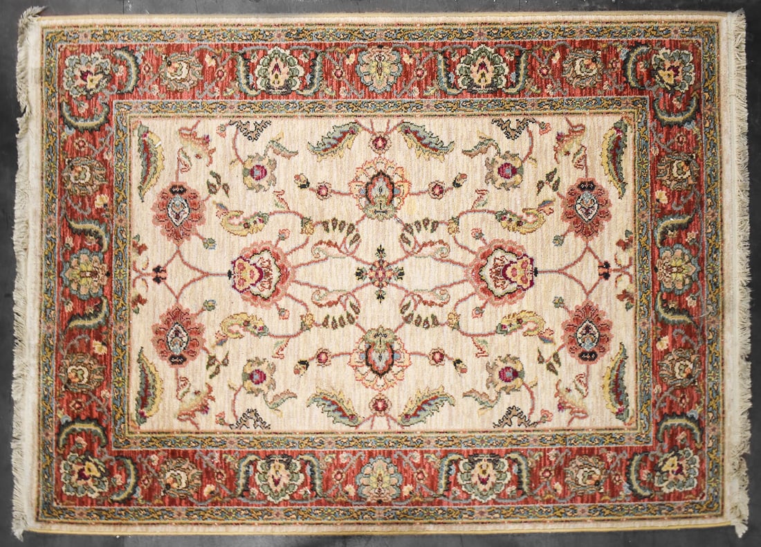 KARASTAN ASHARA "AGRA IVORY" PATTERN WOOL RUG: A Karastan Ashara 100% wool rug in the "Agra Ivory" pattern with a traditional floral design in the field and a thick red border. The rug measures 74" H x 52" W x 0.5" D.