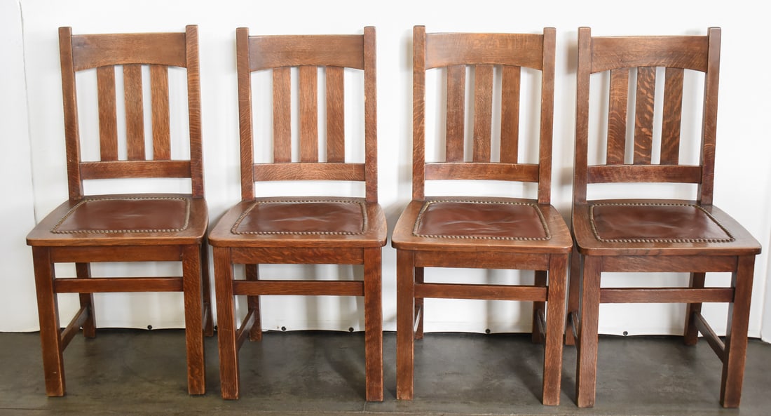 SET OF FOUR ARTS & CRAFTS MISSION OAK LADDER BACK DINING CHAIRS: A set of four Arts & Crafts Mission oak in the manner of Stickley or Limbert ladder-back dining chairs with riveted leather seats. The chairs measure 37" H x 18" W x 16" D. There are no makers mar