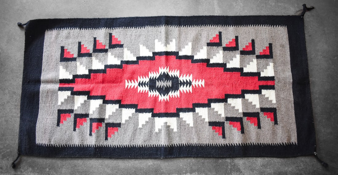 SOUTHWESTERN TRIBAL THROW RUG: Textile has a geometric central pattern featuring the colors black, red and gray. Rug has measurements of 63" H x 32" W x 0.5" D.