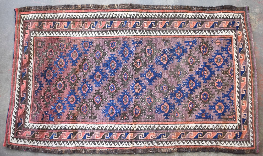 BALUCH WOOL RUG: A Baluch wool rug, circa early-mid 20th century. The rug features a multi-colored geometric design center and a triple running-dog design border. The rug measures 47" L x 29" W x 0.25" D.