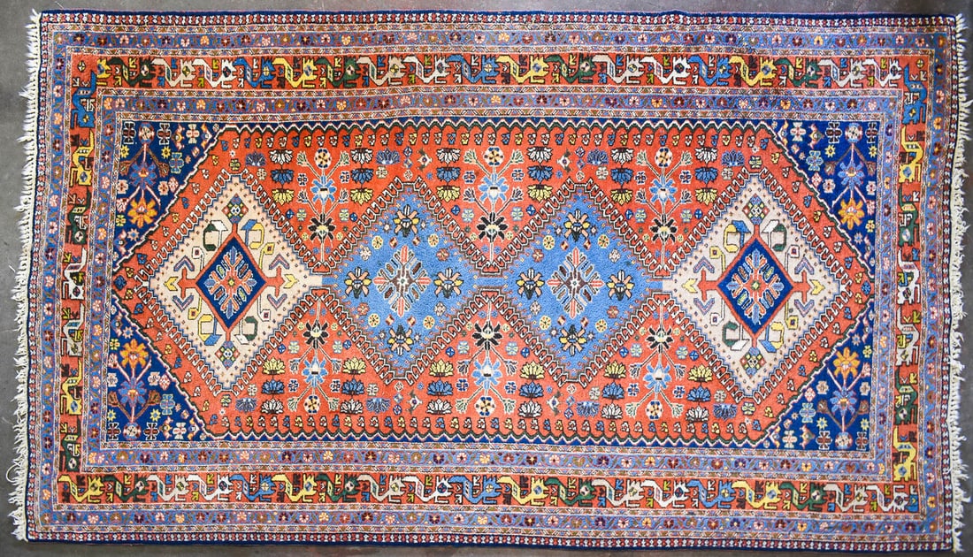 PERSIAN YALAMEH WOOL RUG: A Persian Yalameh wool area rug, likely circa 1940s, featuring four geometric diamond shaped central medallions in beige and light blue colors, dark blue corners, and a very detailed multiple border.