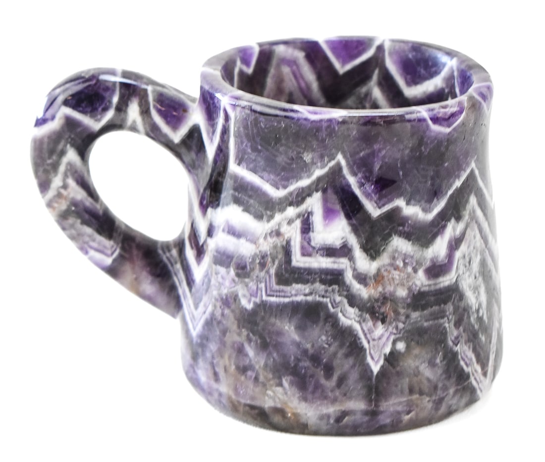 CHEVRON AMETHYST CARVED MUG WITH CARVED LION: A chevron amethyst carved mug with a carving of a lion carved into the side. The mug measures 4" H x 6" W x 4.5" D.
