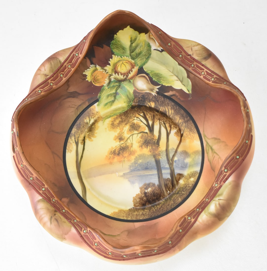 NIPPON MORIMURA BROTHERS HAND-PAINTED MORIAGE RUFFLED BOWL: A Nippon Morimura Brothers hand-painted moriage ruffled bowl featuring a lakeside scene with a raised design, circa 1911-1921. The item measures 4" H, 9" W, 10" D.