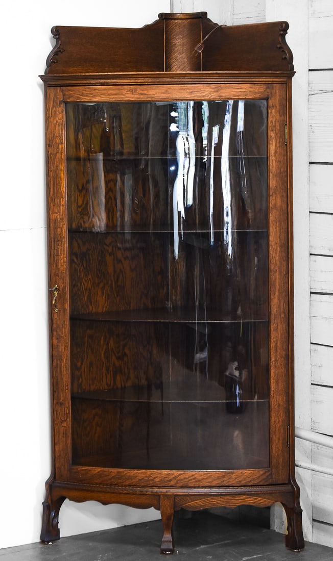 VICTORIAN OAK CORNER LIGHTED CABINET: A lighted Victorian oak corner cabinet with a curved glass door and four adjustable shelves. Measures 58" H 31" W x 19" D.