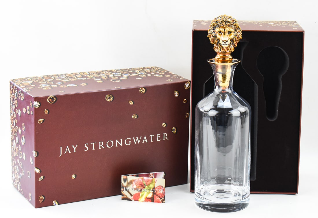 JAY STRONGWATER SWAROVSKI LUTHER LION HEAD DECANTER: A Jay Strongwater Luther lion head decanter featuring Swarovski crystals and a 14K gold paint finish with an original box. The item measures approx. 6.5" H x 13.5" W x 9" D.