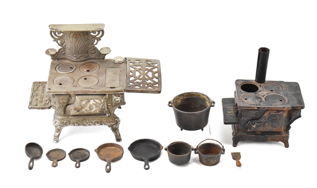 PAIR OF CAST IRON MINIATURE TOY STOVES: A pair of cast iron miniature toy stoves, one by Grand Jewel and one by Daisy. Both circa early 20th century. Includes seven small cast iron pots and pans and a small coal scoop. The largest of the tw