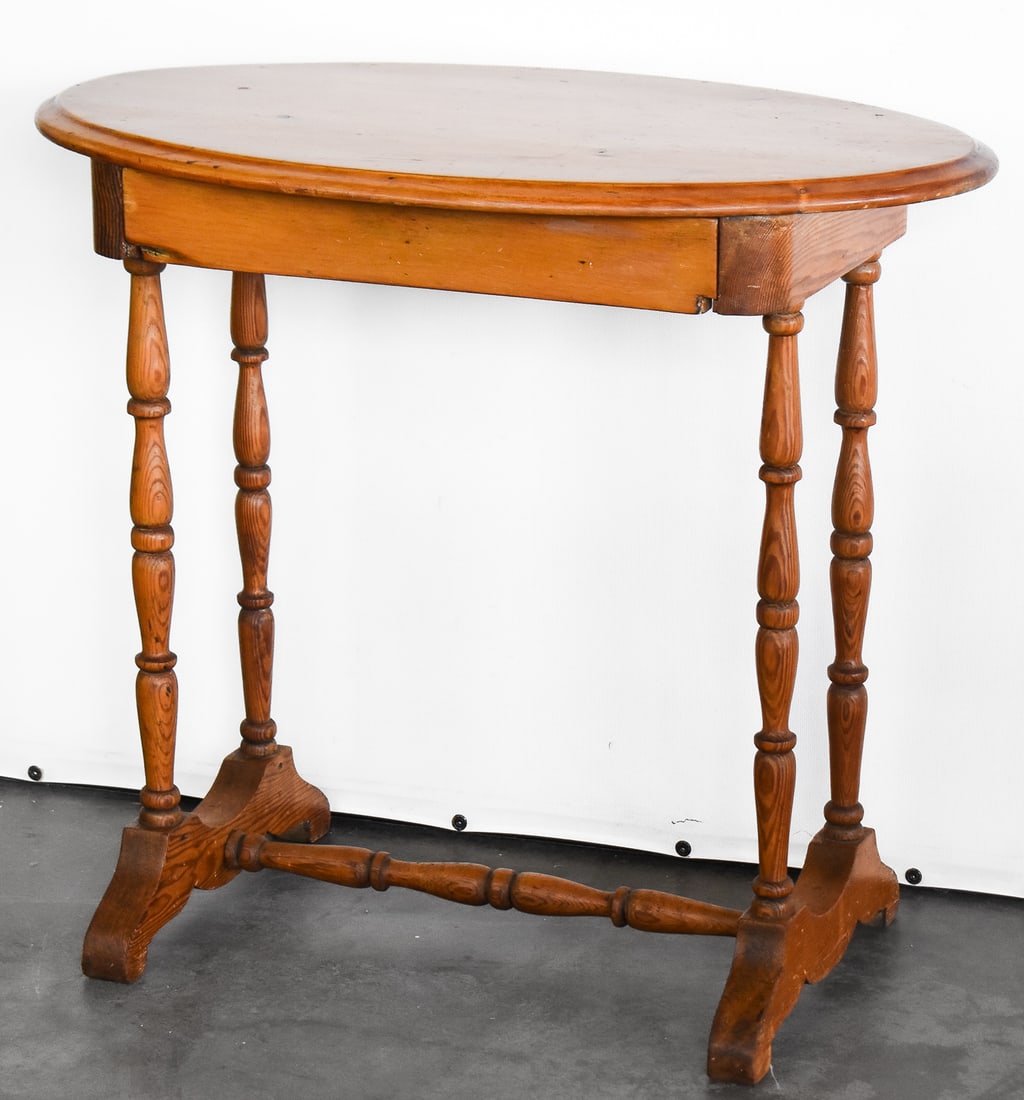 OVAL TOP SIDE TABLE: Table is made of pine wood and features an oval top and spindle legs connected to a trestle base. Table was built circa late 19th century and measures approx. 27.5" H x 30.5" W x 18.5" D.