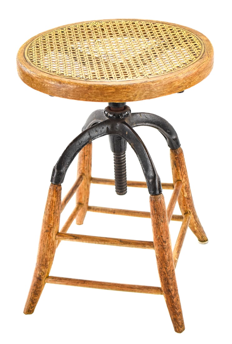 ANTIQUE OAK & CANE INDUSTRIAL DRAFTING STOOL: A circa 1920s-30s oak and cane industrial drafting stool which measures approx. 19.5" H x 14" W x 14" D.