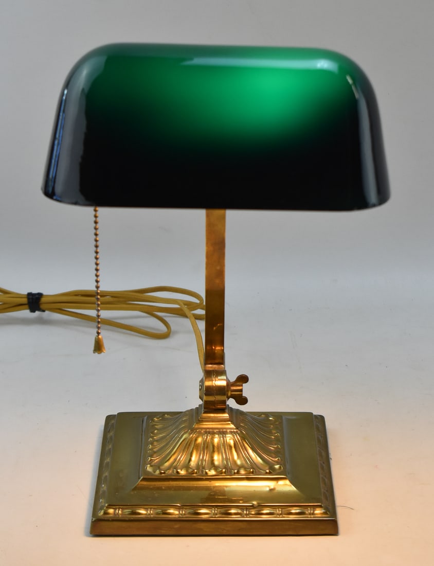 EMERALITE BANKER'S LAMP: This lamp is model number 8734 and produced by H.G. McFaddin & Co. in the 1910s. With a glass shade and brass double knuckle base, this lamp measures approx. 13.5" H x 7" W x 12" D.