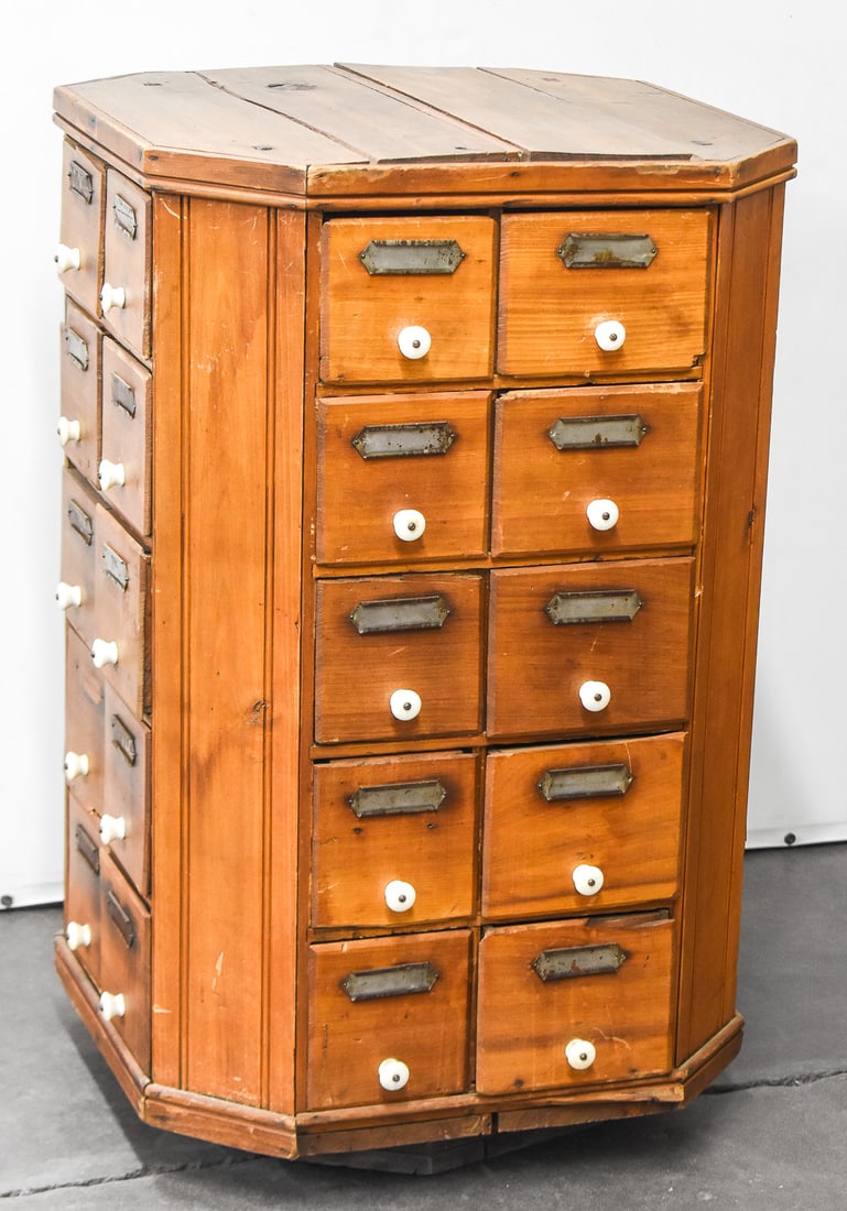 A.R. BROWN ATTRIBUTED REVOLVING HARDWARE CABINET: The cabinet features a compact octagonal design made of oak wood. Each side has 2 rows of 5 drawer of various lengths, all with porcelain handles. The whole cabinet measures approx. 36.5" H x 22.5" W