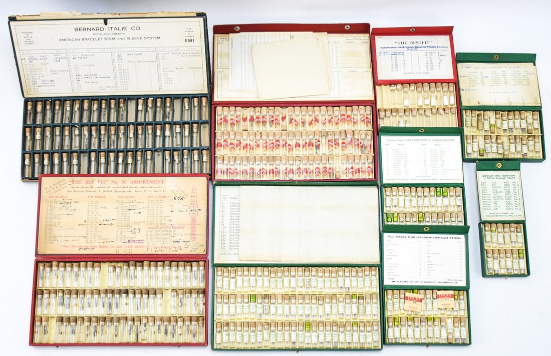 WATCH PARTS: STEMS: Nine cases of watch parts, primarily watch stems with some other assorted gears and parts. One of the cases has empty watch part containers. The watch stems are for the watch bands Benrus, Bulova,