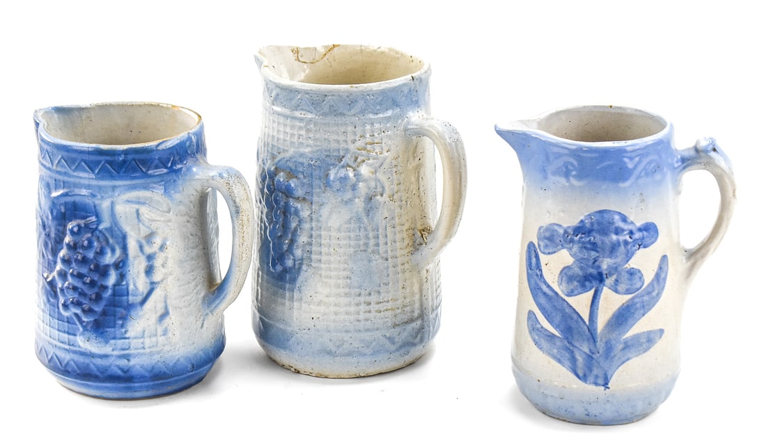 TRIO OF AMERICAN BLUE-AND-WHITE STONEWARE PITCHERS: This lot includes three American blue-and-white salt-glazed stoneware pitchers, from late 19th to early 20th century: 'Grape and Trellis', 'Dutch Windmill', and one featuring a floral motif. The large