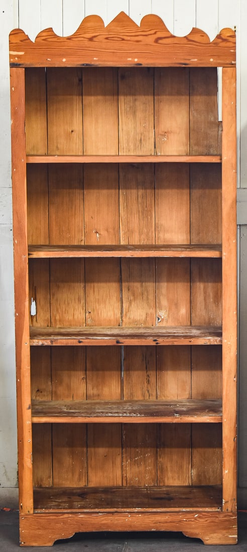 FARMHOUSE STYLE FREE-STANDING PINE BOOKCASE: A Farmhouse style pine bookcase with a scalloped top, late 19th-early 20th century. The item measures approx. 73" H x 30" W x 14" D.