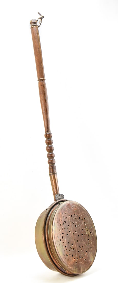 BRASS BED WARMING PAN: This 19th century bed warming pan features a wooden handle and a brass pan with star and floral perforations. The entire pan with the handle measures approx. 42.5" H x 11.5" W x 4.5" D.