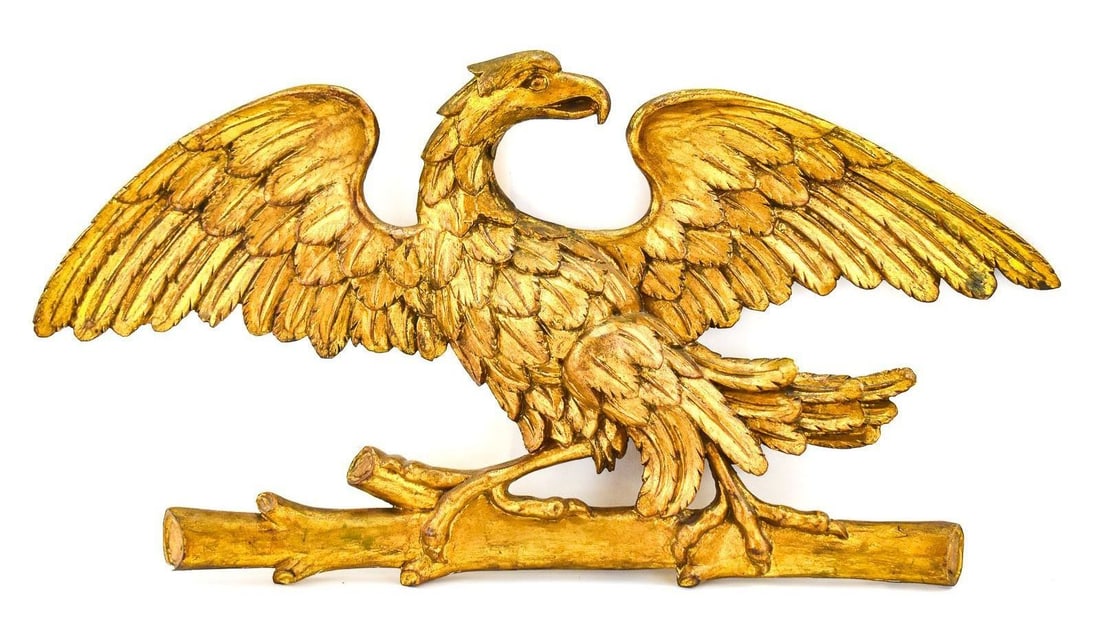 AMERICAN FOLK ART STYLE GILT PERCHED EAGLE: A wall-hanging American folk art style gilt wood-carved eagle perched upon a branch, from mid-20th century. The item measures approx. 19" H x 36" W x 5" D.
