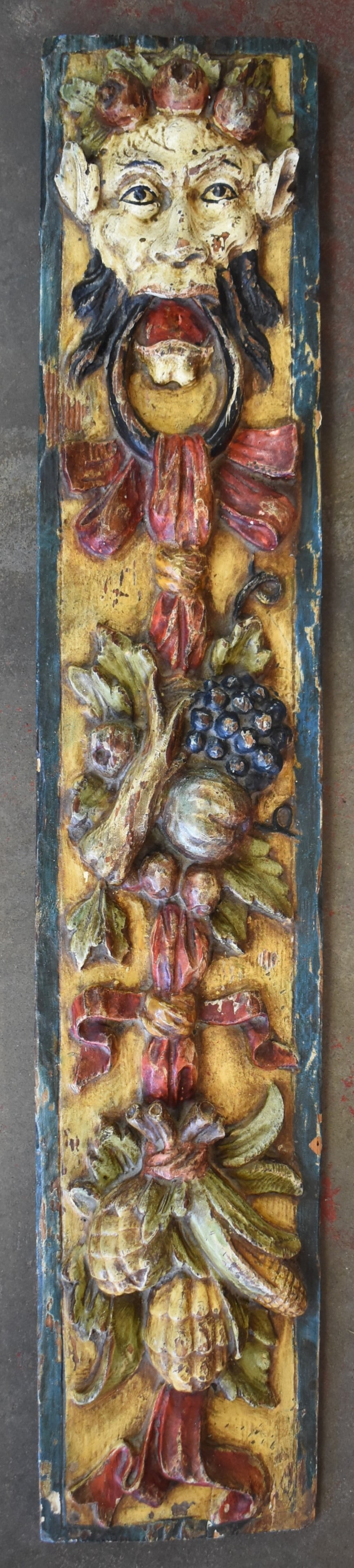 RENAISSANCE REVIVAL STYLE POLYCHROME BACCHUS PANEL: A Renaissance Revival style polychrome-painted wooden carved panel featuring a Bacchus depiction amongst fruit and foliage, from late 19th century. The panel measures approx. 47" H x 9" W x 1" D.