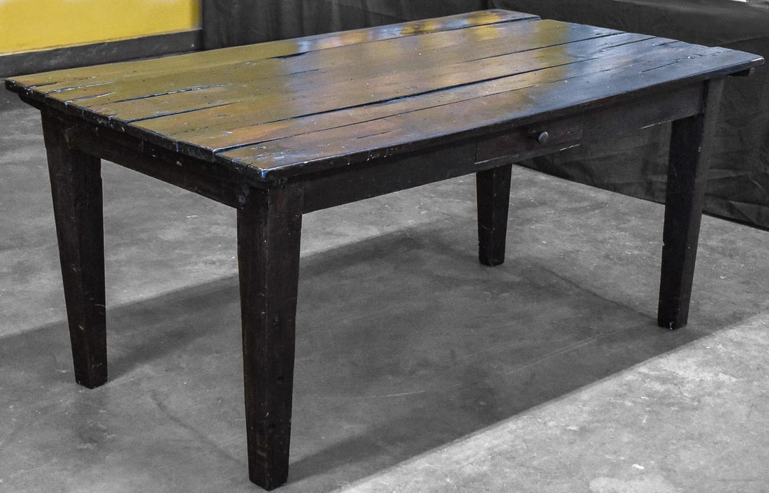 AMERICAN PRIMITIVE-STYLE FARM TABLE; C. LATE 19TH CENTURY: An American Primitive-style farm table made of dark stained wood with a single central drawer and tapered legs, from late 19th century. The table measures approx. 31" H x 72" W x 40" D.