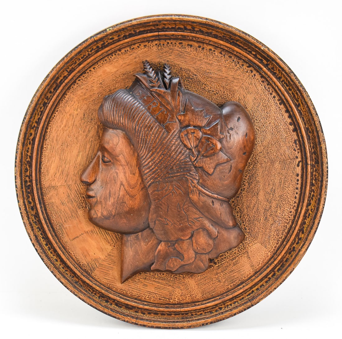WOODEN MEDALLION PLAQUE WITH LADY LIBERTY: This hand-carved wooden medallion plaque features a relief portrait of a personified Liberty in 19th century American folk art style. It is unsigned and measures approx. 17.5" H x 17.5" W x 3" D.