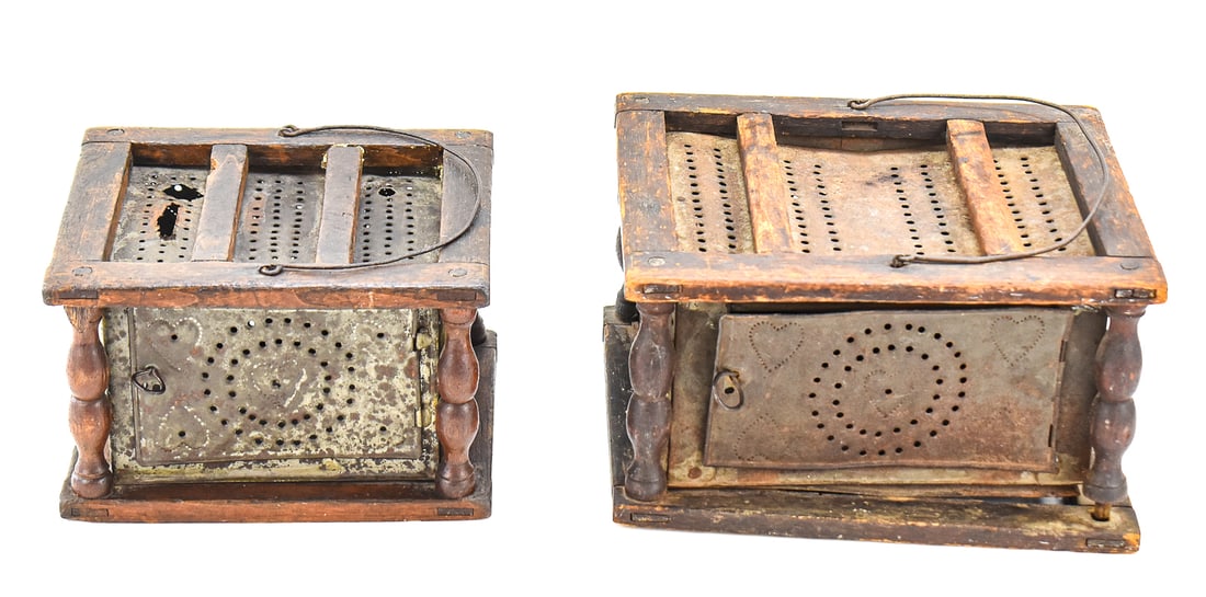 EARLY AMERICAN PUNCHED TIN HEART-DESIGNED FOOT WARMERS: This lot includes two early American punched tin and turned wood foot warmers featuring a heart-design, from the early-mid 19th century. The largest foot warmer includes the original coal box and